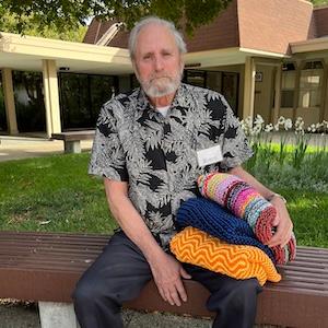 Photo of Milt Gentry sitting in Trinity Court holding three blankets he made