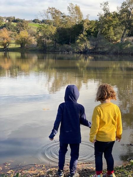 Two children seen from behind skipping a stone into a pond