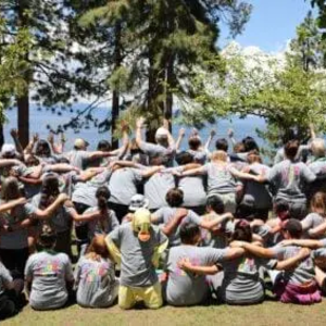 Group photo of dozens of campers facing away from the camera with their arms around each other's shoulders looking out over the lake