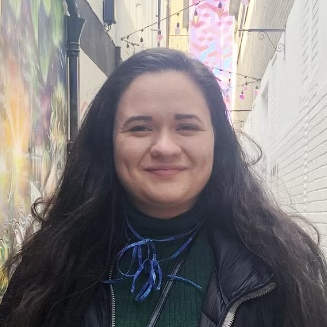 Smiling headshot of Jenna Burkhalter standing beside a painted brick wall