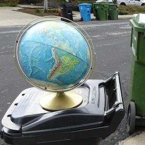 Photo of a globe sitting on top of a household trash can at the curb on trash day