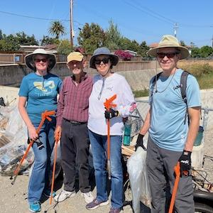 Photo of four smiling adults wearing sunhats and holding cleanup wands