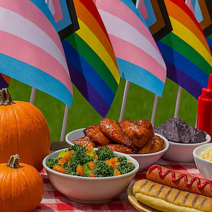 Picnic food on a table with a row of LGBTQ Pride flags behind