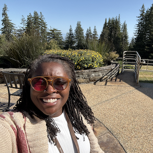 selfie photo of Pastor Annanda at Mt Madonna retreat with the courtyard around her and trees and blue sky behind