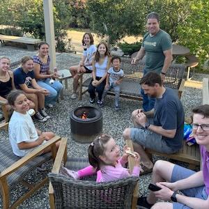 Photo of families roasting marshmallows around the fire pit on the patio at church
