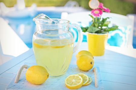 pitcher of lemonade and lemons and a potted flower on a light blue picnic table