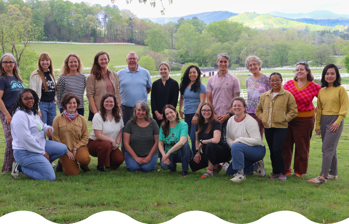 A large group of adults pose for a photo with a scenic farm landscape in the background.