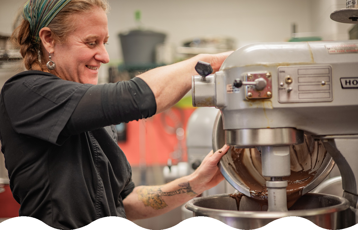 A cook pours brown batter into a large industrial mixer