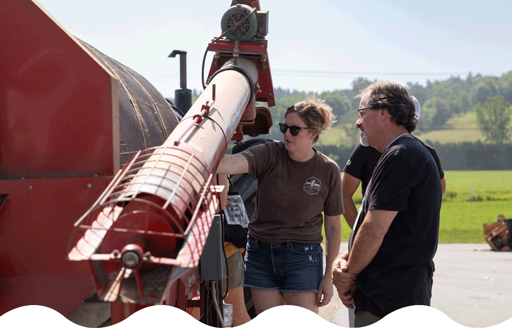 Two individuals are examining a large red industrial machine used in grain processing.