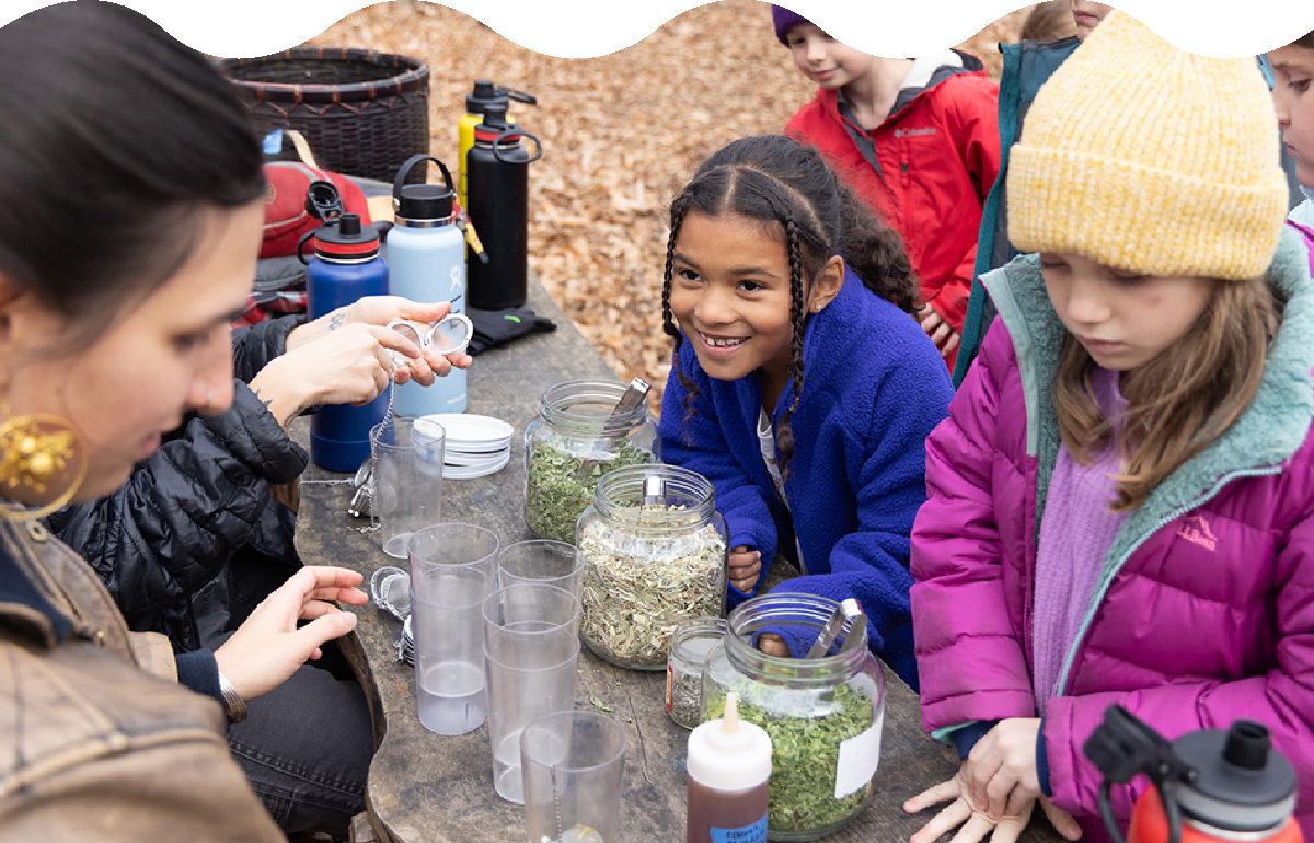 A group of young children make tea at an outdoor table