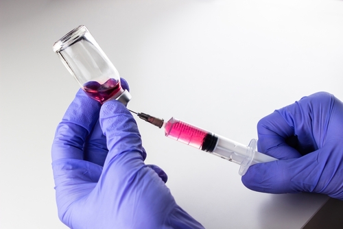 a disposable syringe with a needle and an ampoule with red  vitamin B12  liquid in male hands in blue  lilac  nitrile gloves.  On a white background_ lots of empty space