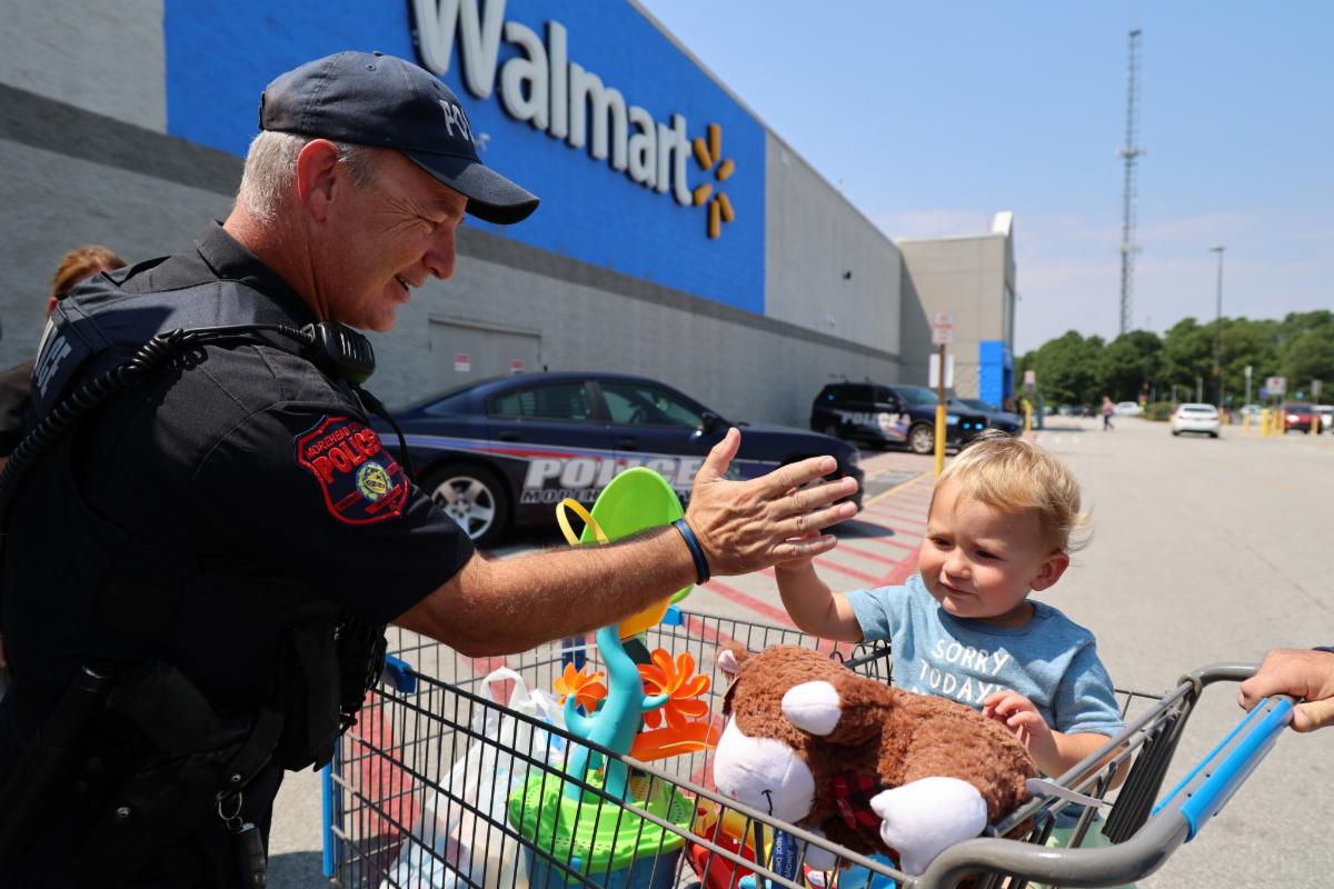 A police officer gives a high five to a young child in a shopping cart outside of Walmart