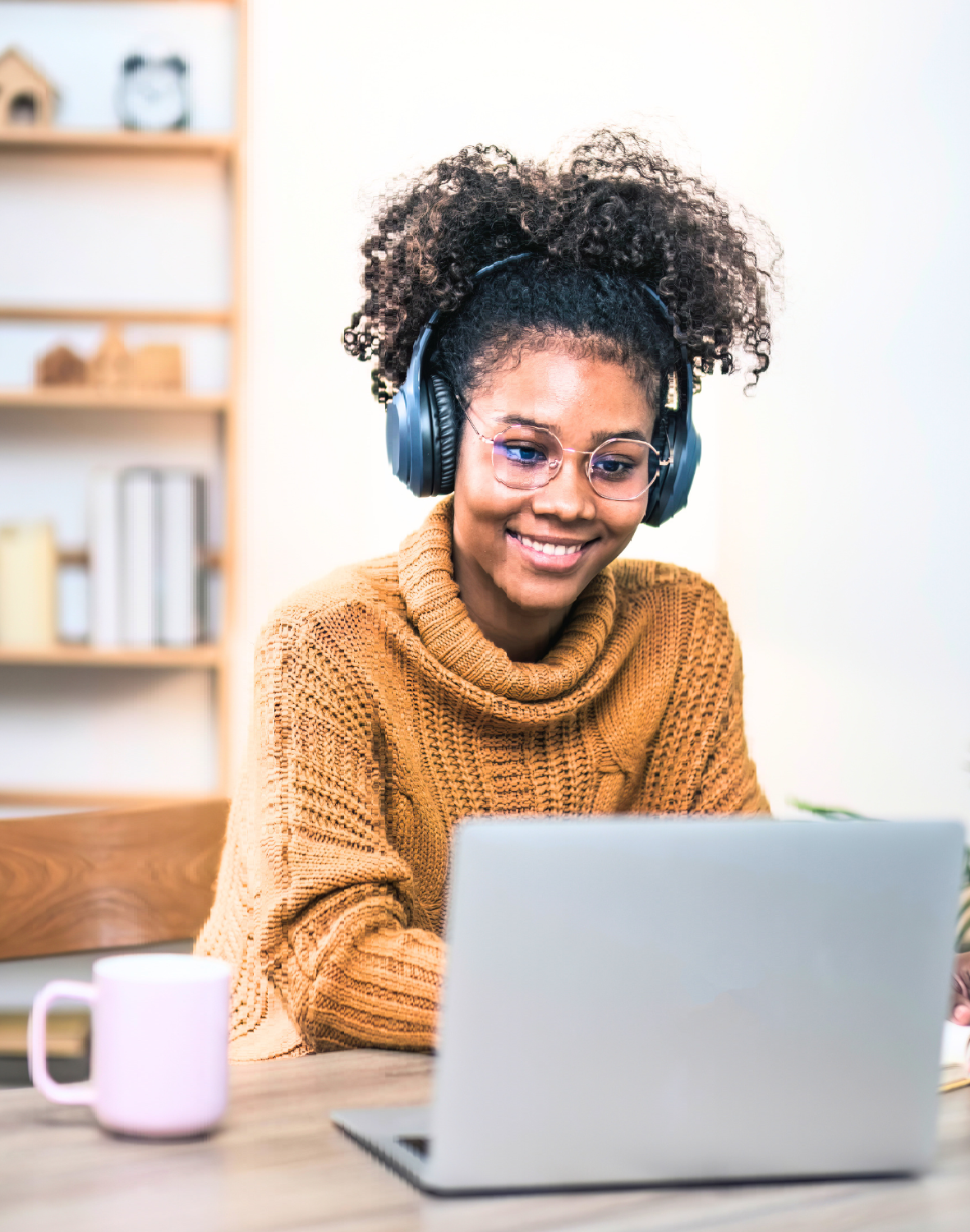 Young woman with headphones on, looking at laptop and smiling.