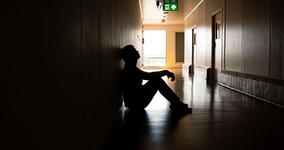 Male school student sitting alone in a dark hallway