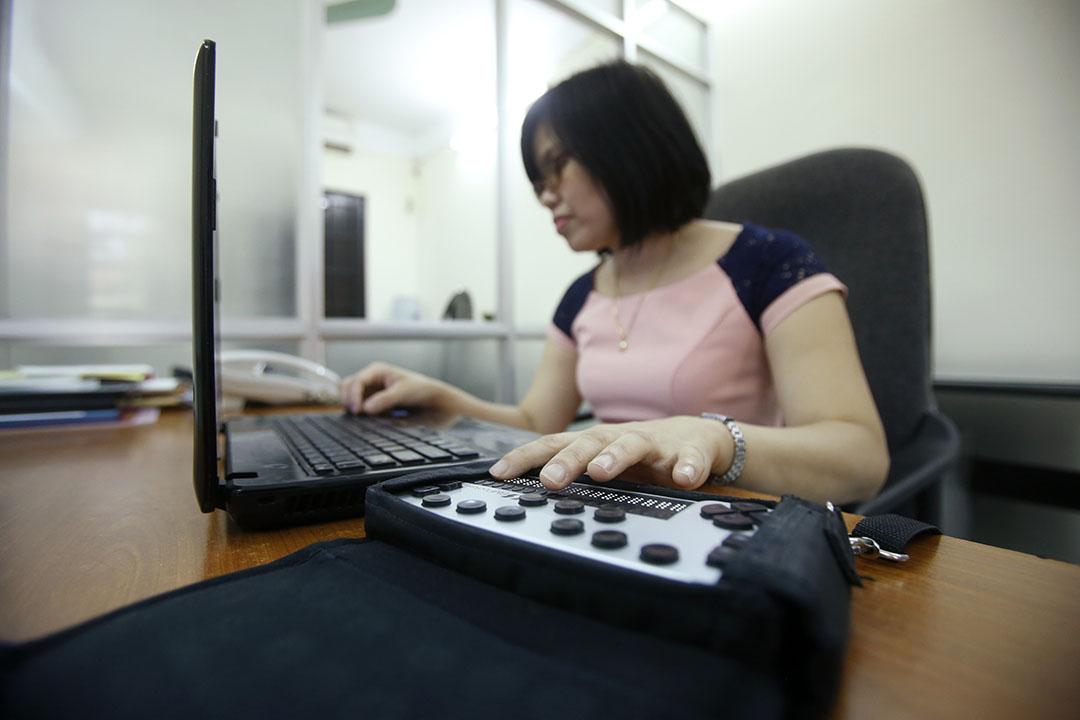 asian woman using braille reader with computer