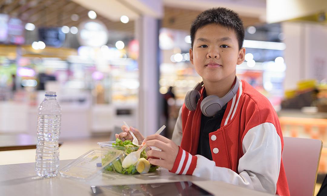teen boy eating a healthy salad in a food court