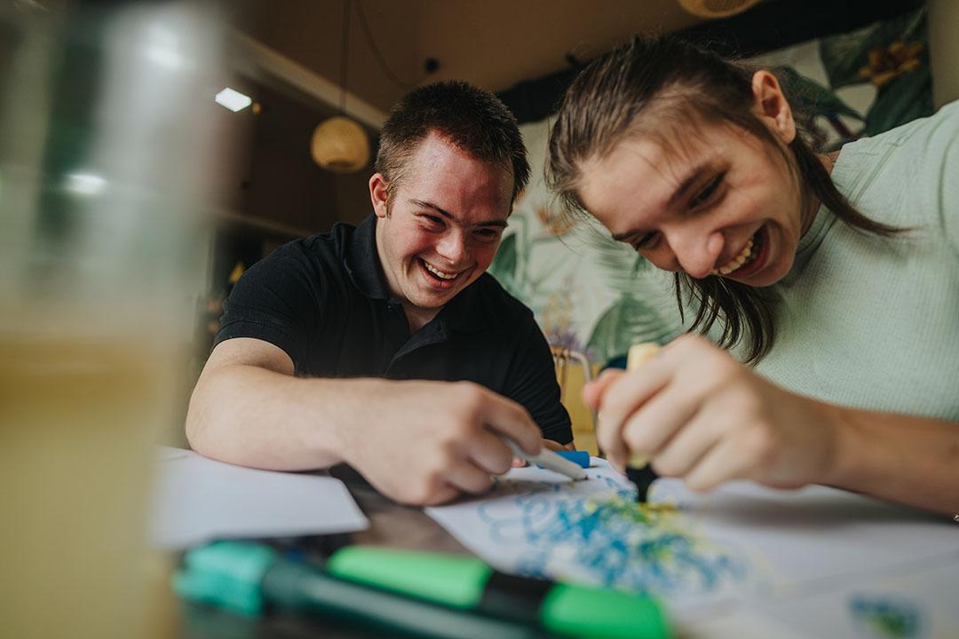 Teen boy with Down syndrome and a girl in a wheelchair collaborate on an art project