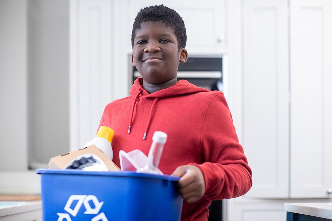 Teen boy working in a recycling center carrying a blue collection bin.
