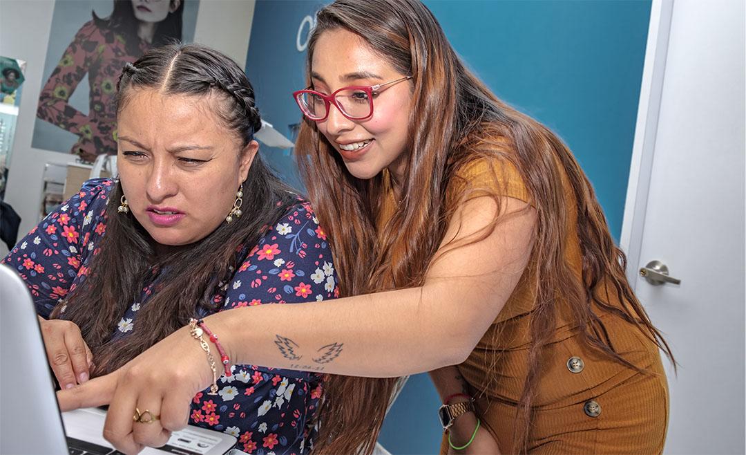 2 hispanic woman working at a desk together to figure out a problem related to benefits