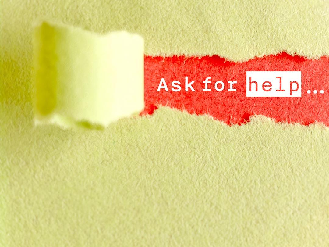 Paper sign made by tearing away an upper layer of yellow paper to reveal a lower layer of red paper with the words "Ask for Help." 