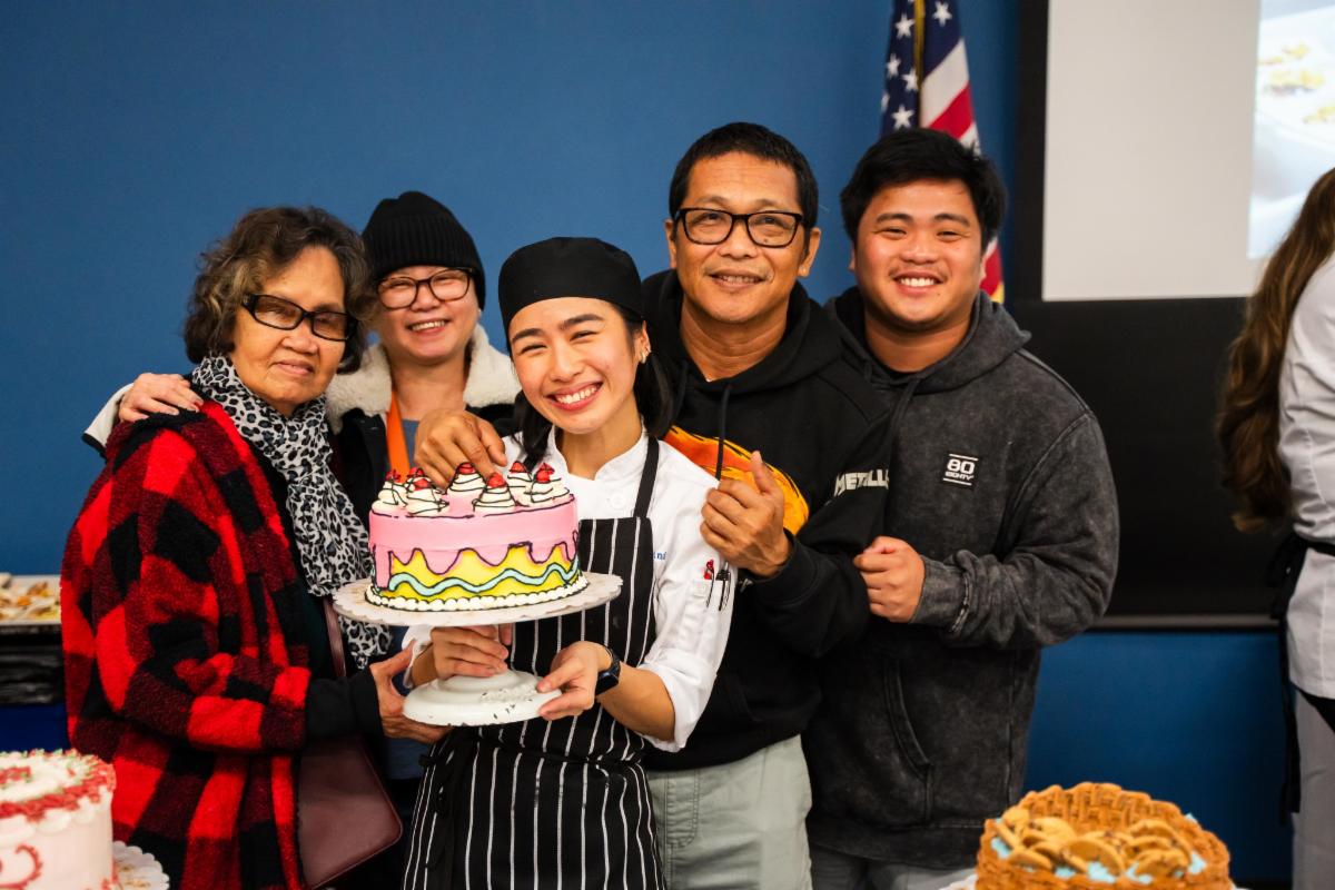 A chef with her family holding a pink cake decorated with strawberries and chocolate.