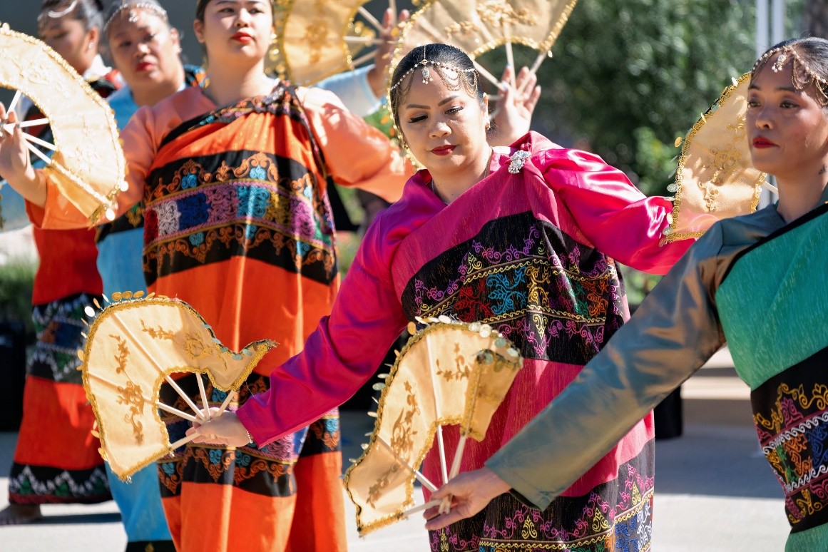 Ladies in bright colored robes perform a dance with gold fans