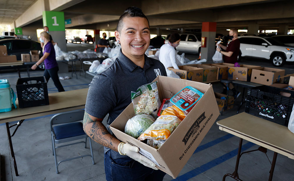 A volunteer carries a box of food at a distribution event.