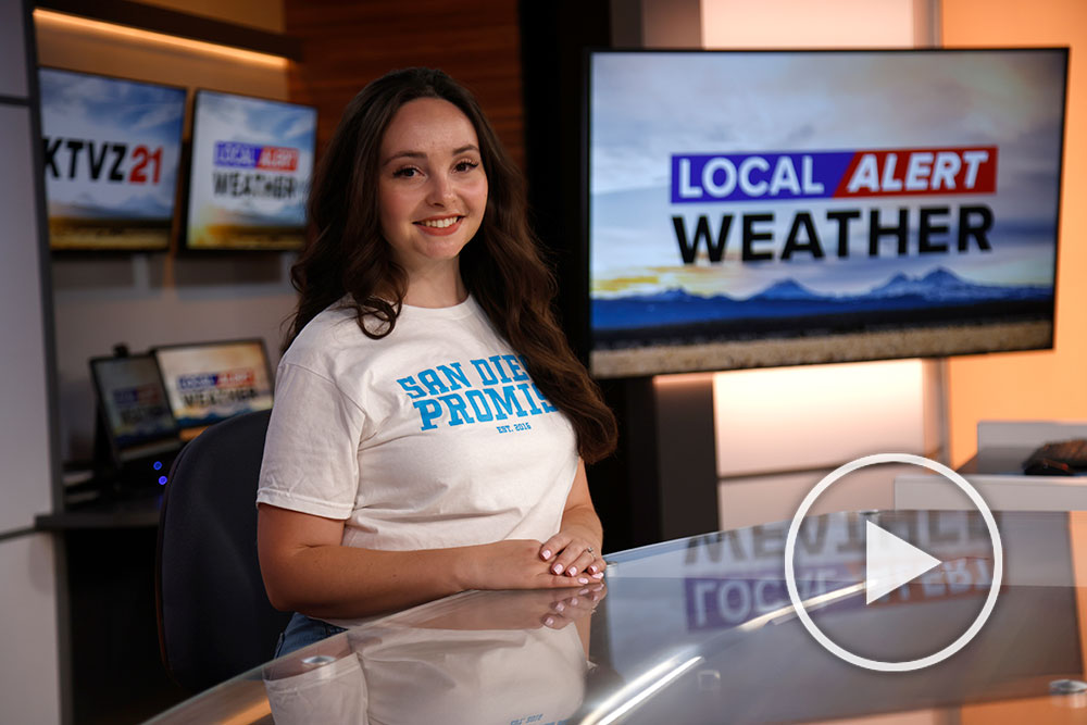Alum Jillian Fortner wears a San Diego Promise tee shirts at the news desk in the tv studio where she works
