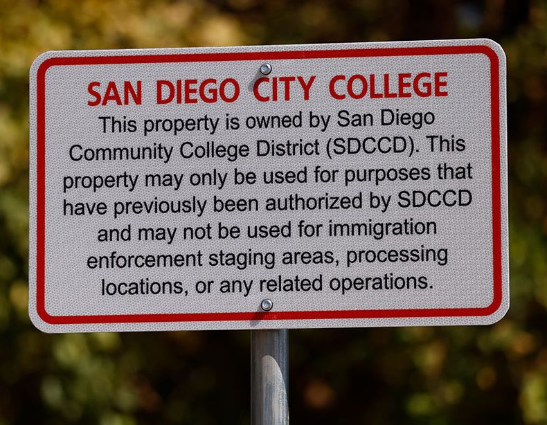 A white and red sign along a pathway at City College.