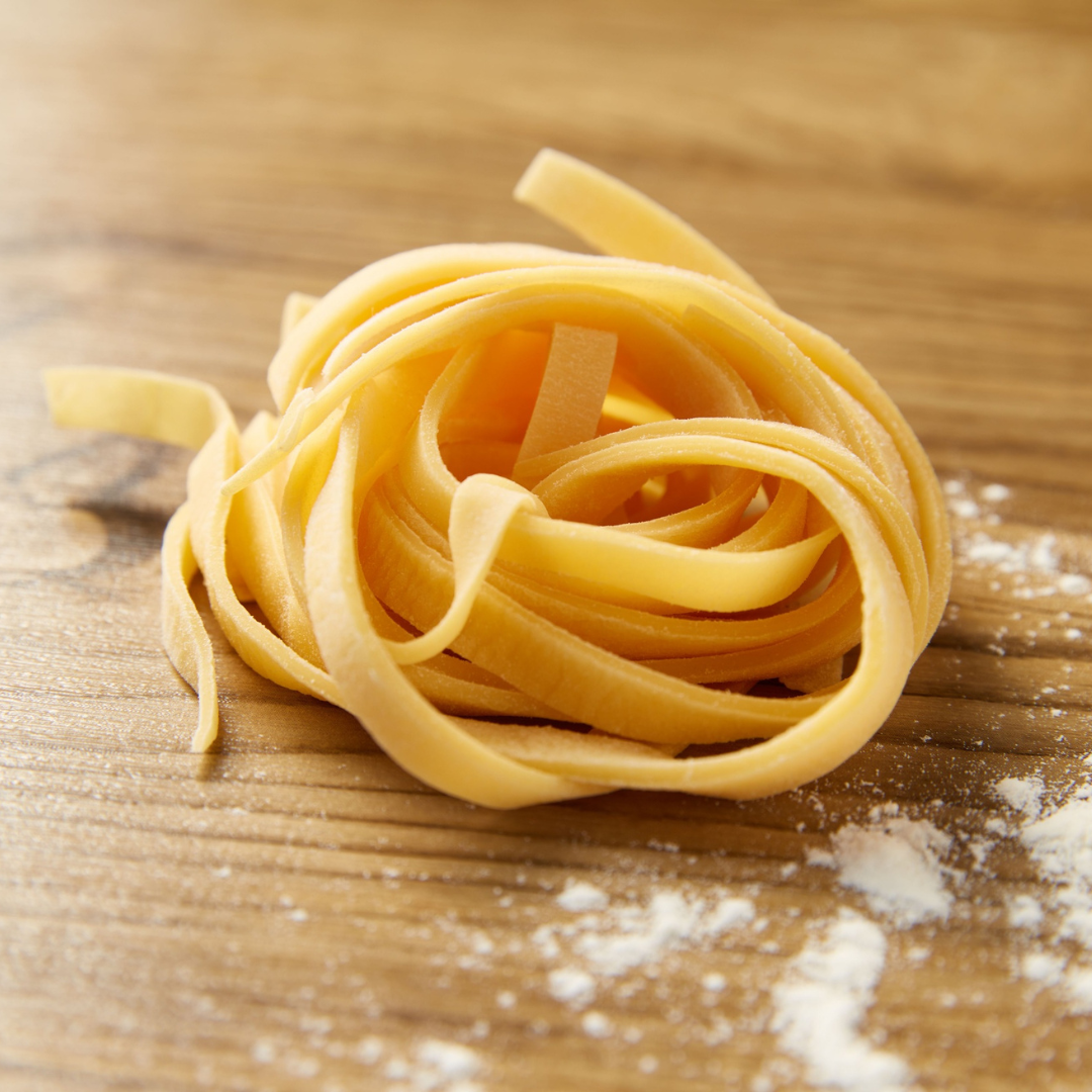 Fresh pasta on a wooden cutting board and a sprinkle of flour