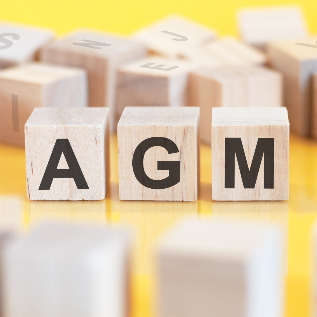 Wooden blocks with letters on them sit on a table top. Letters on three blocks in the middle of the image spell out "AGM."