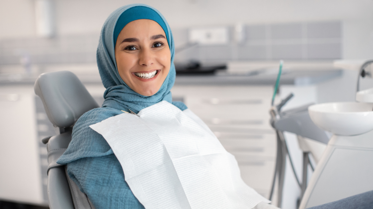Patient wearing headscarf smiles while in dental chair.