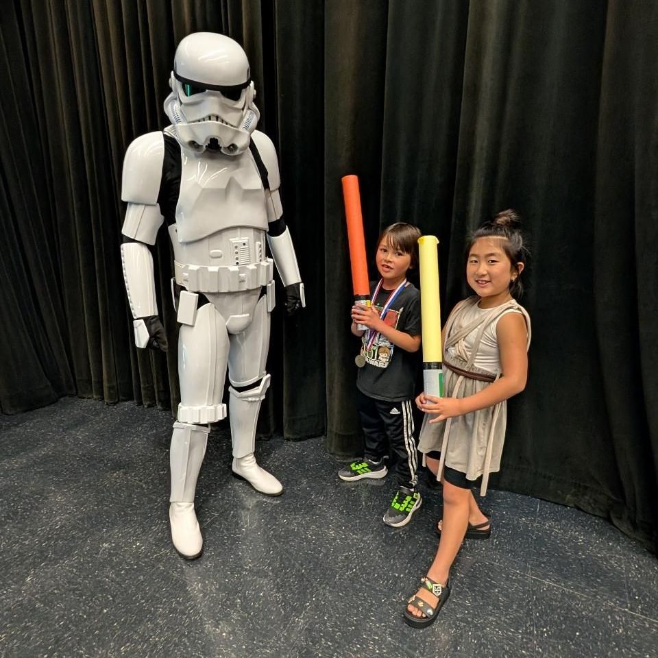 Kids with light sabers standing next to Strom Trooper