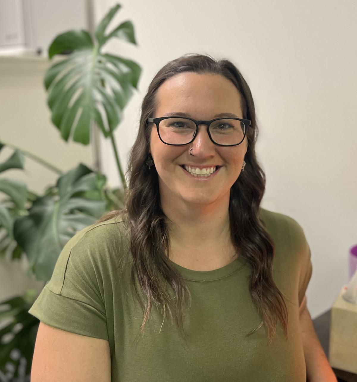 The massage therapist Christine with glasses, long hair with plants behind
