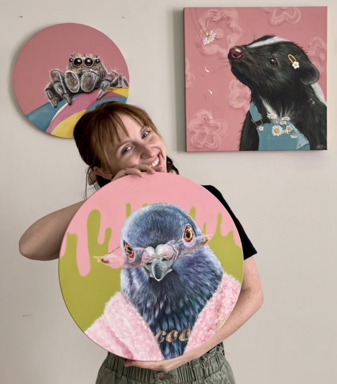 Artist Becca Lanes holds one of her animal paintings with two hung behind her
