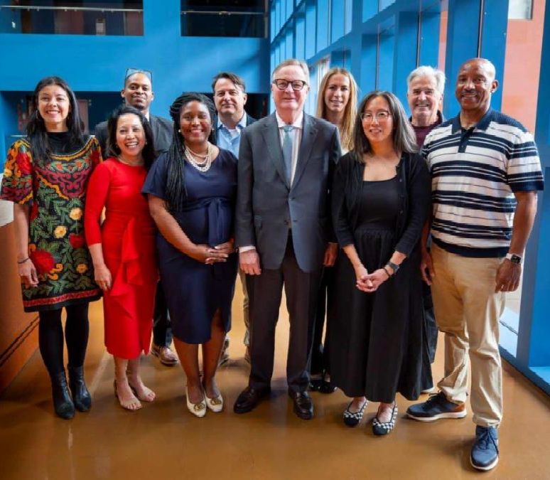 Image of honorees at past Blanket Ceremony, standing with colorful blankets around shoulders and person looking on in background. All are smiling.