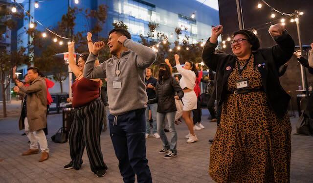 People dancing outside in evening under festive lights. The mood is joyous.