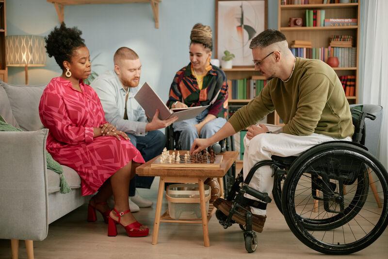 Group of four adults sitting around a coffee table playing games. There are two wheelchair users.