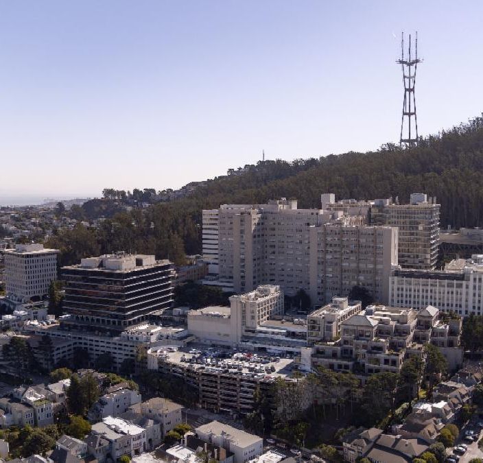 Bird's eye view photo of UCSF Parnassus campus and surrounding neighborhood with Sutro Tower in upper right and blue sky with light fog.