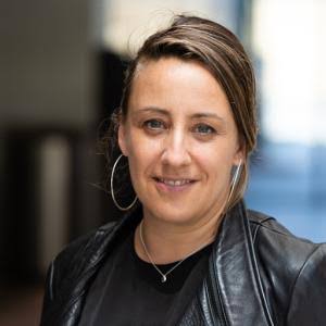 Headshot photo of Cecile Puretz wearing black jacket and hoop earrings smiling. 