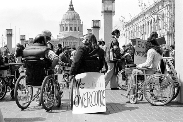 Black & white photo featuring various individuals in wheelchairs with posters, protesting in front of a Federal building in San Francisco.