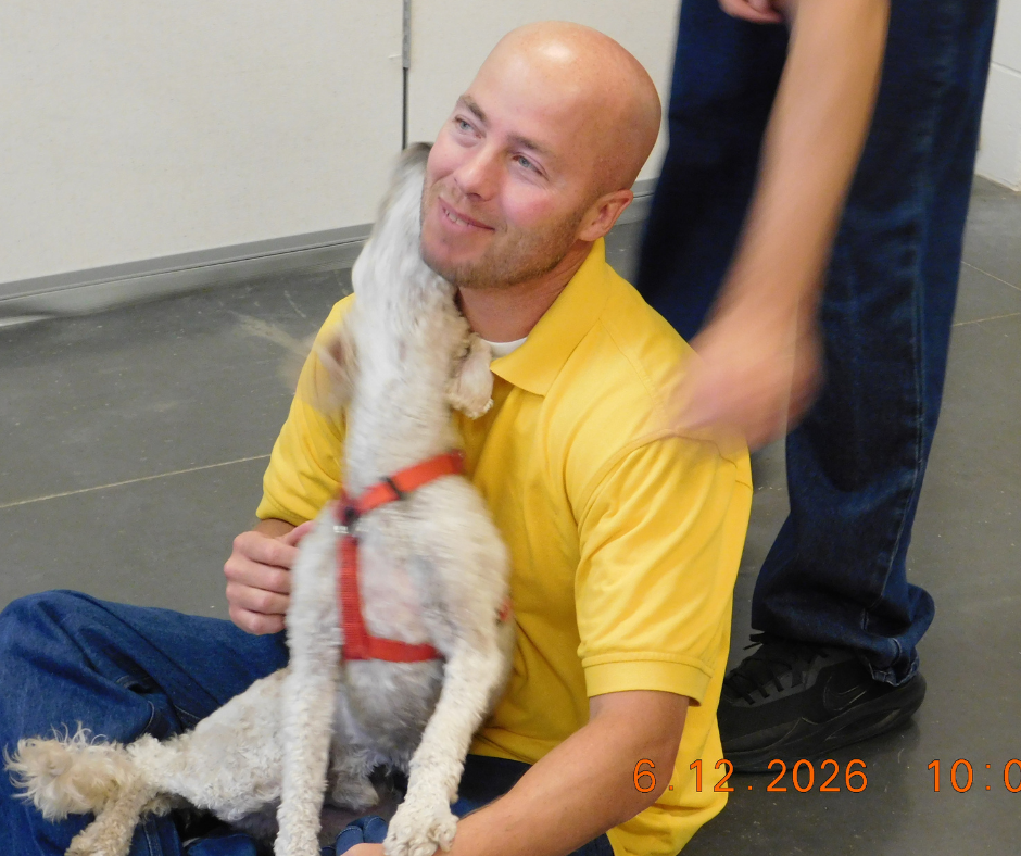 Russell beams as Astro, a cream colored doodle sits in his lap. 