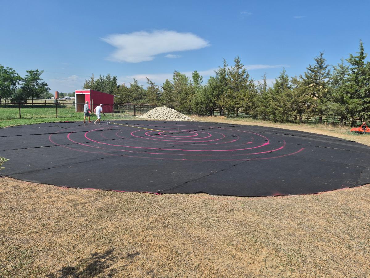 A circle of black weed cloth has red lines on it. 