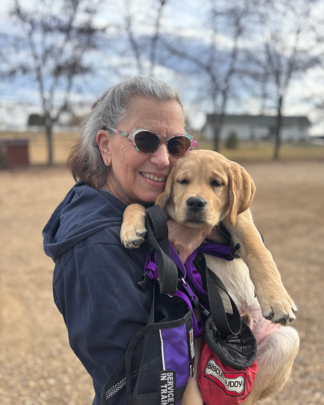 Goose's puppy raiser smiles while holding the 12 week old lab puppy.