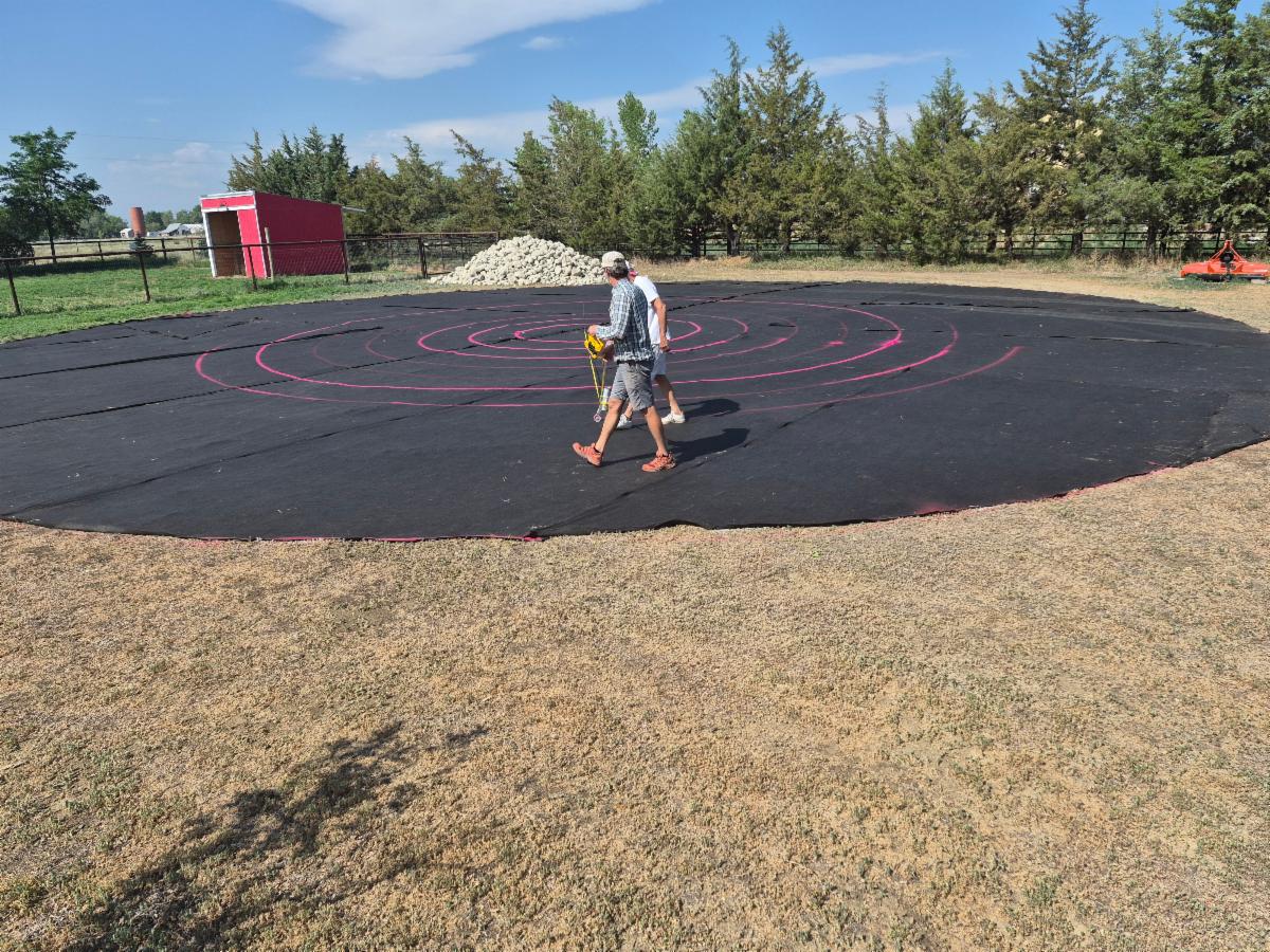 A circle of black weed cloth is on the ground as someone walks on it. 