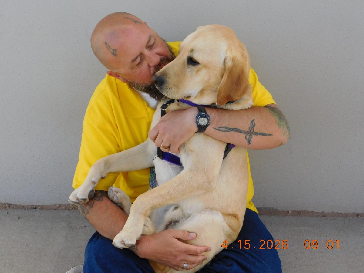 A inmate in yellow holds Fortune a yellow lab. Kissing him lovingly. 