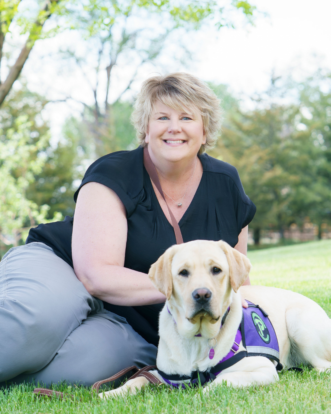 Client Kari smiles next to her hearing dog a yellow lab named Doc.