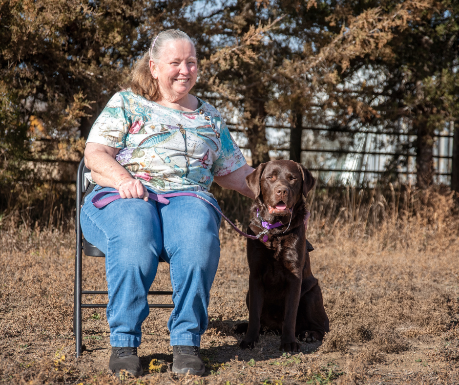 Beth sits next to her hearing dog Pruitt a chocolate lab. 