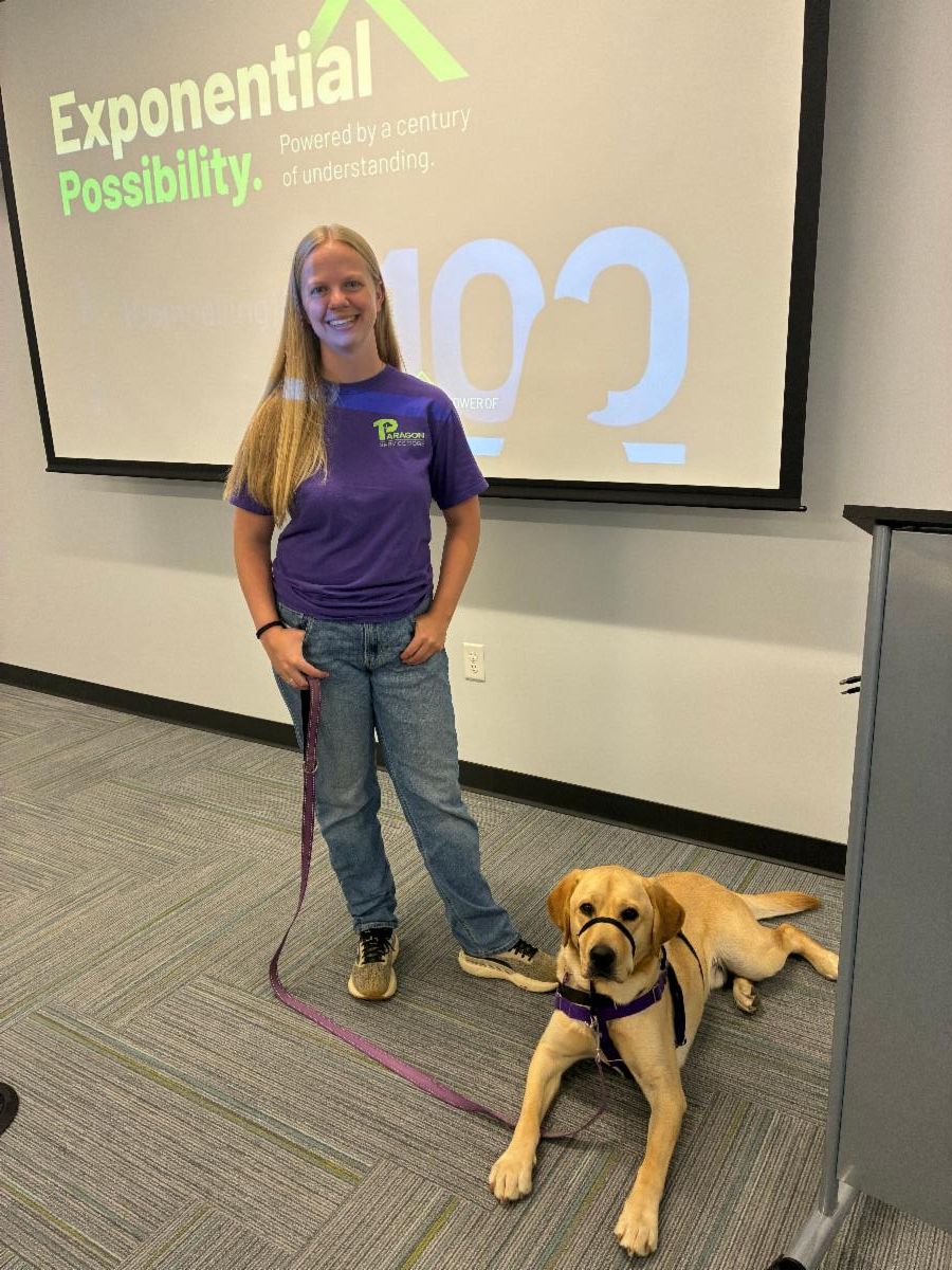 Staff member, Chloe stands smiling next to a yellow lab named Fortune. 