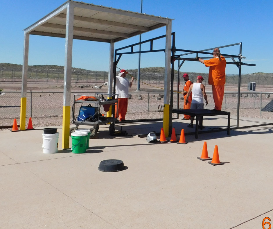 Four inmates work outside setting up a structure base. 